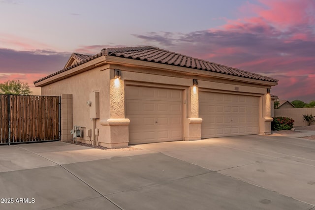 view of property exterior with concrete driveway, stucco siding, fence, and a tile roof
