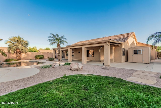 rear view of house featuring stucco siding, a patio area, a tile roof, fence, and a lawn