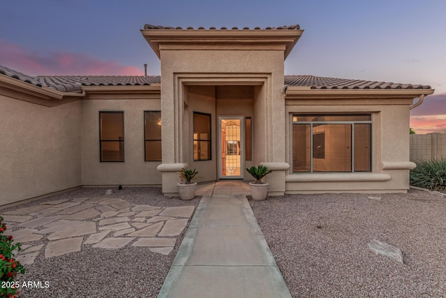 view of exterior entry featuring a patio, a tiled roof, and stucco siding