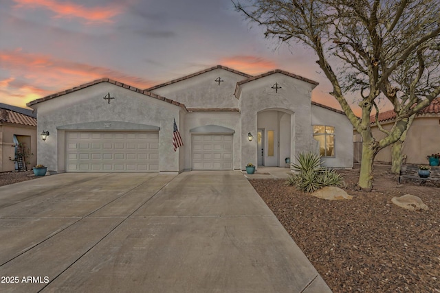 mediterranean / spanish house featuring a tile roof, concrete driveway, a garage, and stucco siding