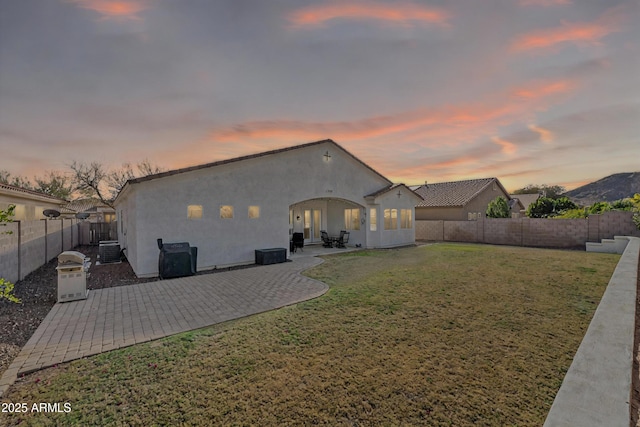 rear view of property with stucco siding, a lawn, a fenced backyard, and a patio area