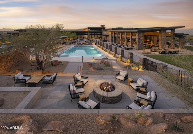 pool at dusk featuring fence, a fire pit, a patio, and a community pool