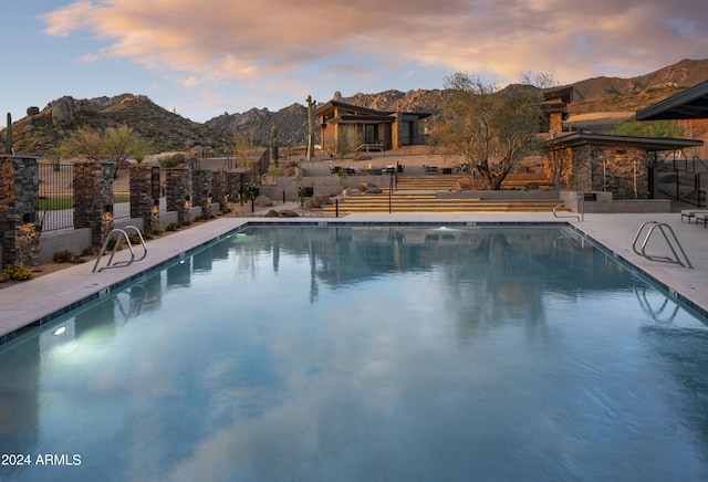 pool at dusk with a patio area, a community pool, fence, and a mountain view