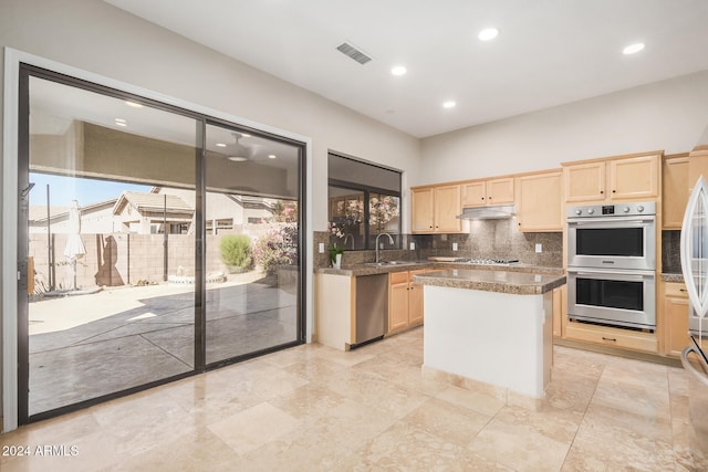 kitchen with stainless steel double oven, a kitchen island, gas stovetop, light brown cabinets, and decorative backsplash