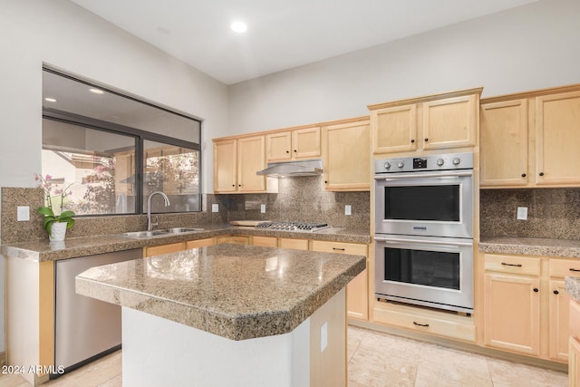 kitchen with tasteful backsplash, light brown cabinetry, sink, double oven, and a center island