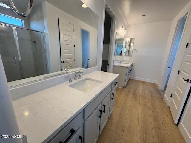 bathroom with hardwood / wood-style floors, baseboards, a stall shower, and a sink