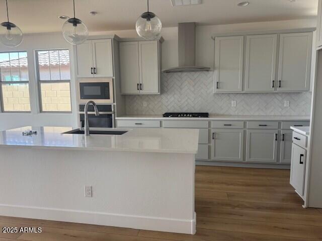 kitchen featuring wall chimney range hood, light countertops, stainless steel oven, and a sink
