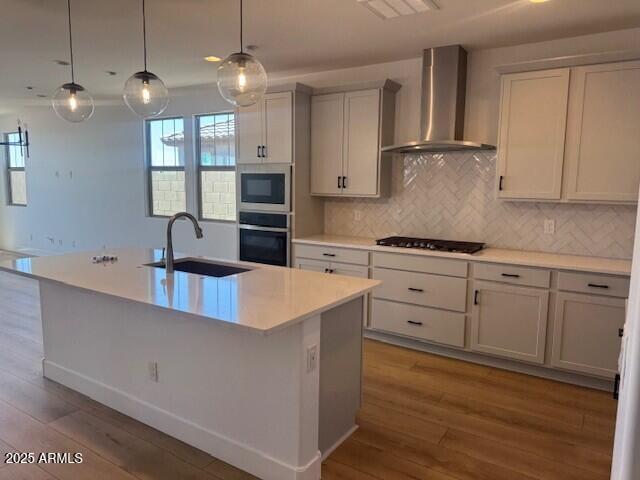 kitchen with wall chimney range hood, a sink, light countertops, black gas cooktop, and wood finished floors