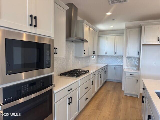 kitchen featuring recessed lighting, stainless steel appliances, light countertops, and wall chimney range hood