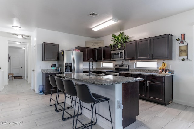 kitchen featuring dark brown cabinetry, a breakfast bar, sink, appliances with stainless steel finishes, and an island with sink