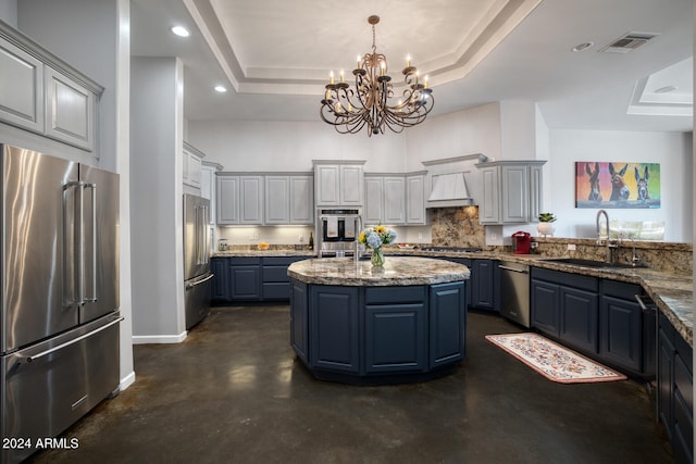 kitchen with a raised ceiling, appliances with stainless steel finishes, an inviting chandelier, and stone counters