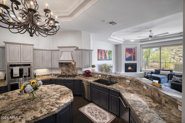 kitchen with gray cabinets, ceiling fan with notable chandelier, and a raised ceiling