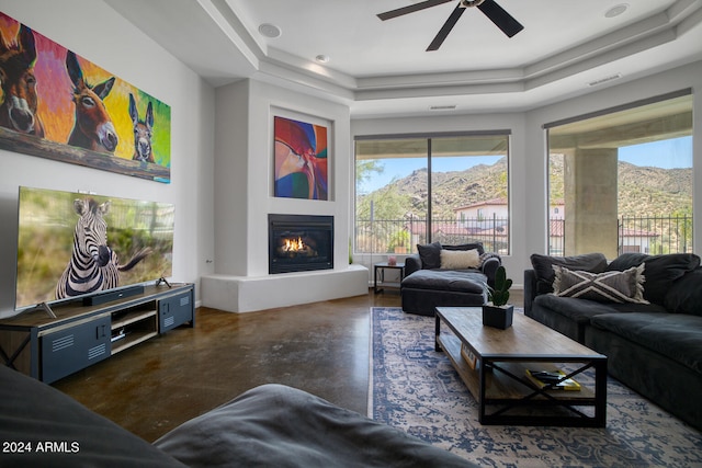 living room with a raised ceiling, ceiling fan, and a mountain view