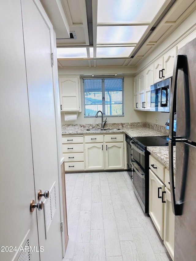 kitchen featuring light hardwood / wood-style floors, light stone countertops, sink, and appliances with stainless steel finishes