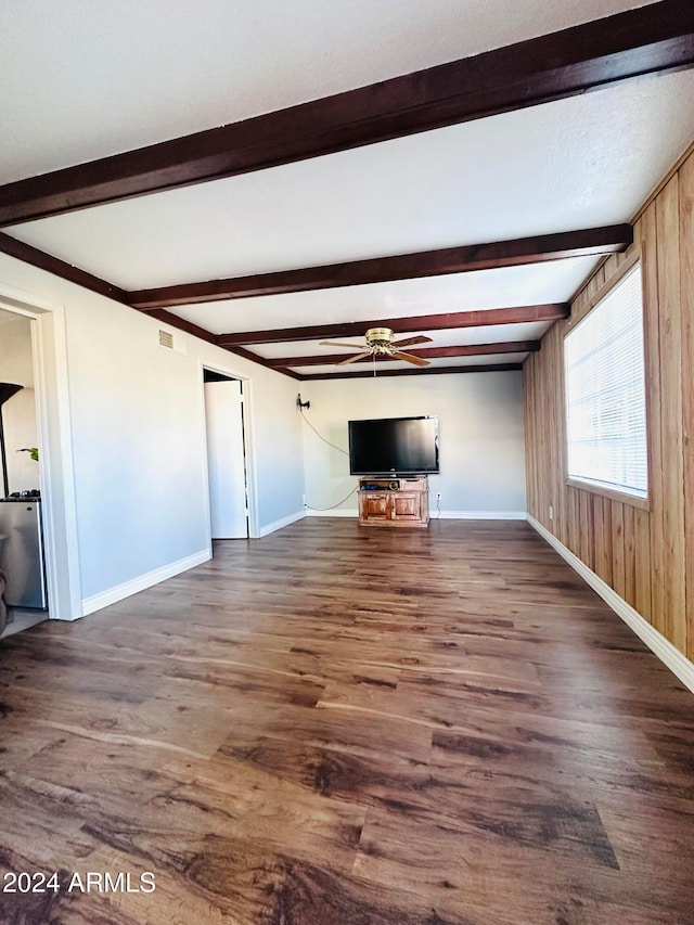 unfurnished living room with beamed ceiling, dark hardwood / wood-style flooring, ceiling fan, and wood walls