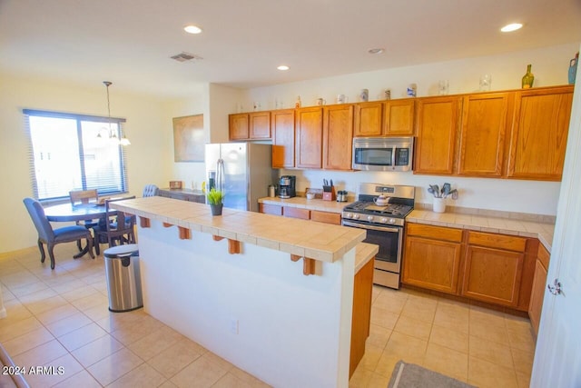 kitchen featuring a kitchen breakfast bar, decorative light fixtures, appliances with stainless steel finishes, tile counters, and a kitchen island