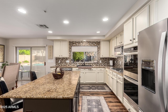 7247 W Buckskin Trl, Peoria, AZ 85383 - kitchen featuring appliances with stainless steel finishes, a kitchen island, light stone countertops, dark wood-style flooring, and decorative backsplash