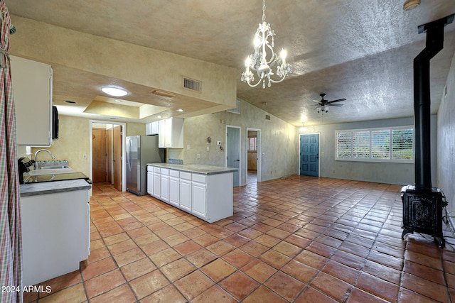 kitchen with stainless steel refrigerator, ceiling fan with notable chandelier, white cabinetry, hanging light fixtures, and a wood stove