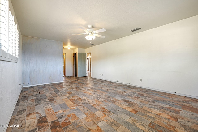 spare room featuring ceiling fan, dark tile flooring, and a textured ceiling