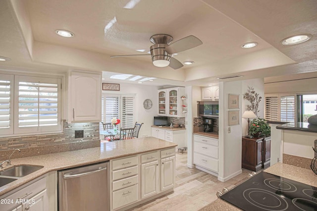 kitchen featuring stainless steel dishwasher, light wood-type flooring, backsplash, and a tray ceiling