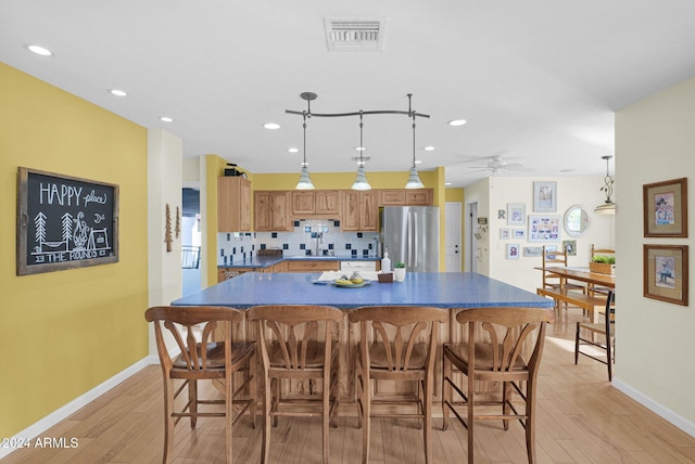 kitchen featuring stainless steel refrigerator, ceiling fan, a center island, tasteful backsplash, and light wood-type flooring