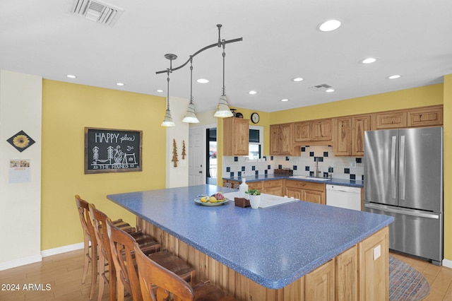 kitchen featuring pendant lighting, white dishwasher, decorative backsplash, stainless steel fridge, and light wood-type flooring