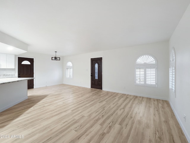 unfurnished living room featuring an inviting chandelier and light hardwood / wood-style flooring