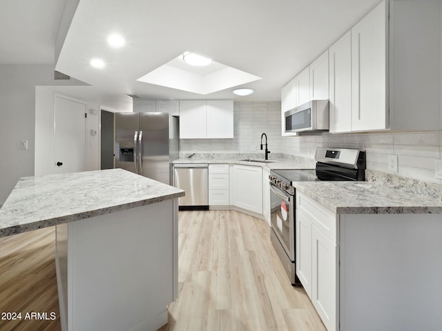 kitchen with a skylight, white cabinetry, decorative backsplash, and appliances with stainless steel finishes