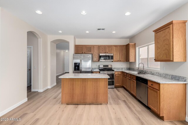 12238 W Monroe St, Avondale, AZ 85323 - kitchen with stainless steel appliances, a sink, a center island, arched walkways, and light wood-type flooring