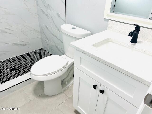 bathroom with toilet, vanity, a tile shower, and tile walls