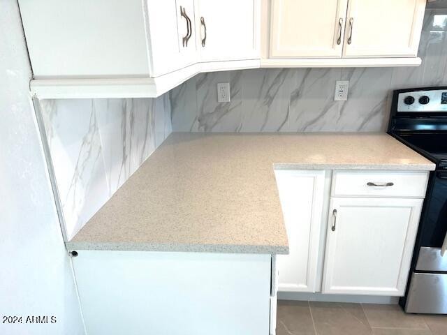 kitchen featuring light tile patterned flooring, light stone countertops, white cabinets, decorative backsplash, and electric stove