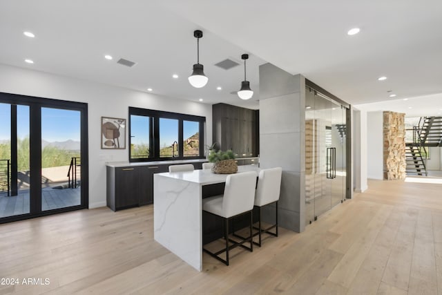 kitchen with light wood-type flooring, decorative light fixtures, a center island, and light stone countertops