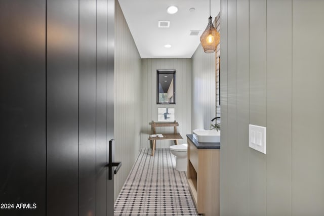 bathroom with toilet, vanity, and wood walls