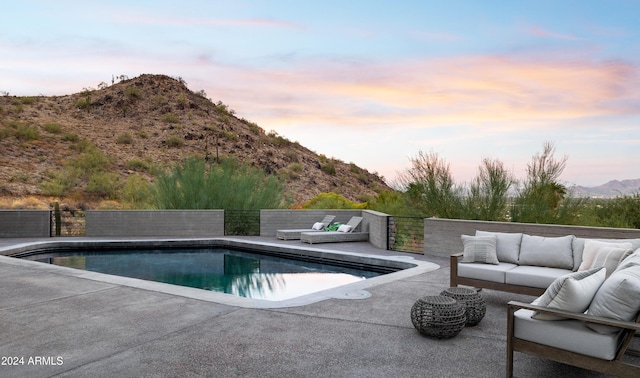 pool at dusk featuring a mountain view, a patio, and an outdoor hangout area