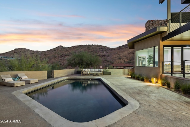 pool at dusk with a mountain view, a patio area, and outdoor lounge area