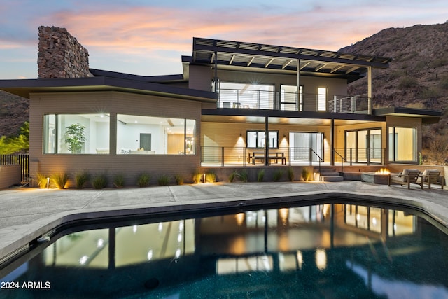 back house at dusk with a mountain view, a patio, and a balcony