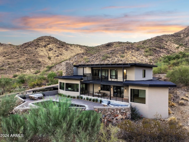 back house at dusk featuring a patio area, a balcony, and a mountain view