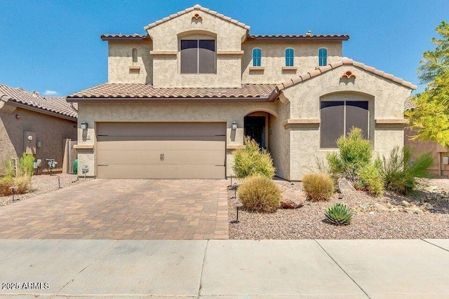 mediterranean / spanish-style house featuring a garage, a tile roof, decorative driveway, and stucco siding