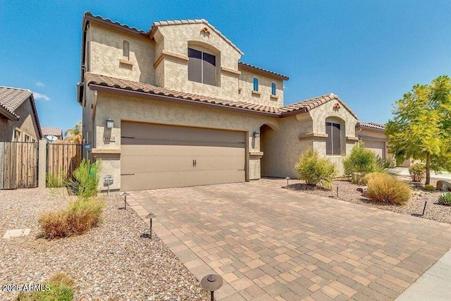 mediterranean / spanish-style home with a garage, decorative driveway, fence, and stucco siding