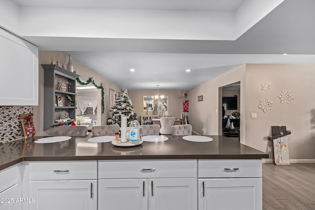 kitchen featuring tasteful backsplash, white cabinets, kitchen peninsula, an inviting chandelier, and light hardwood / wood-style flooring