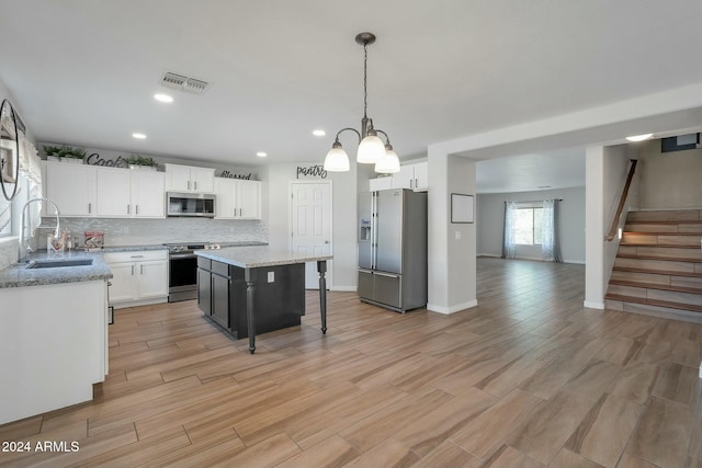 kitchen with appliances with stainless steel finishes, light wood-type flooring, sink, pendant lighting, and white cabinets