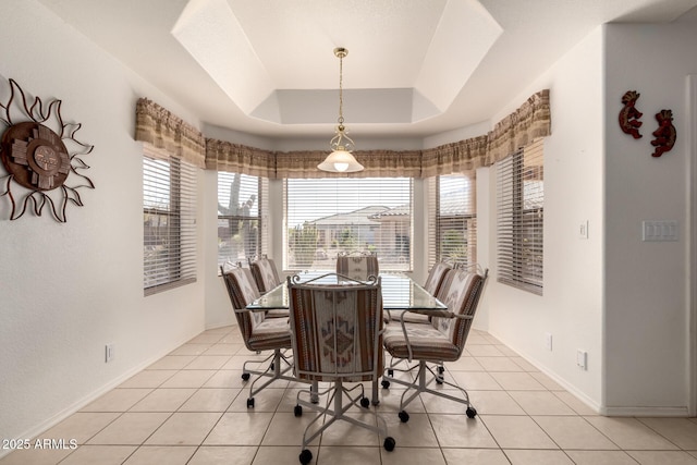 tiled dining room with a raised ceiling and a healthy amount of sunlight