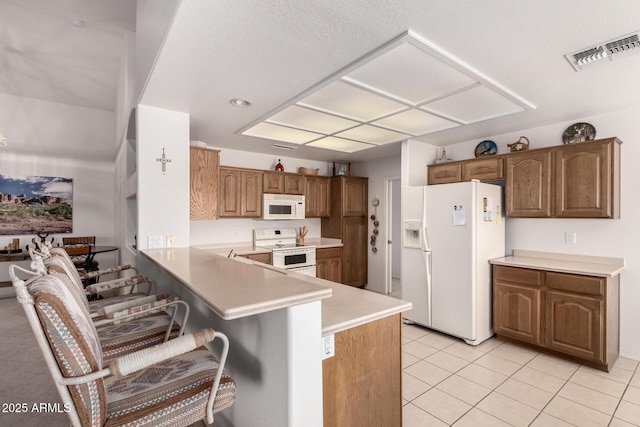 kitchen featuring white appliances, a kitchen bar, kitchen peninsula, and light tile patterned floors