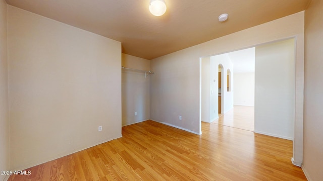 unfurnished room featuring arched walkways and light wood finished floors