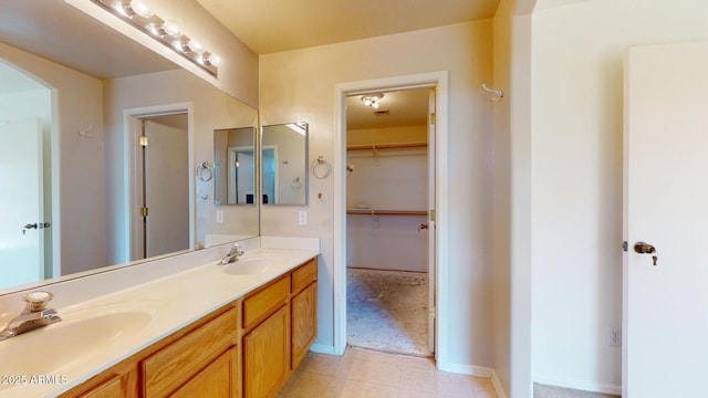 bathroom with a sink, a walk in closet, baseboards, and double vanity