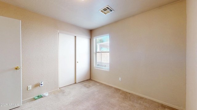 unfurnished bedroom featuring visible vents, carpet floors, a closet, and a textured wall