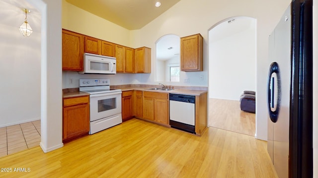 kitchen featuring white appliances, brown cabinetry, a sink, light countertops, and light wood-type flooring