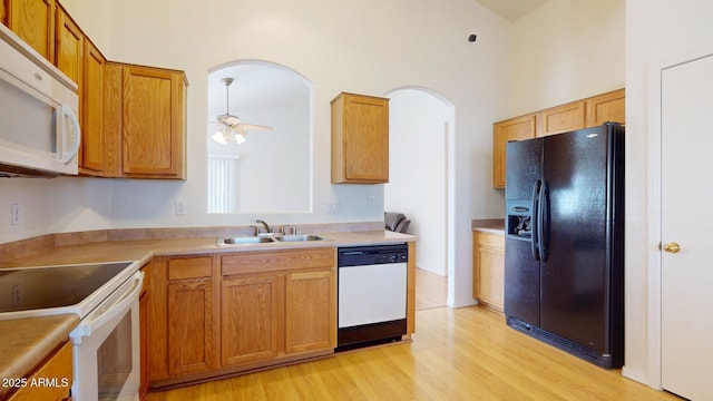 kitchen featuring white appliances, light wood finished floors, arched walkways, ceiling fan, and a sink