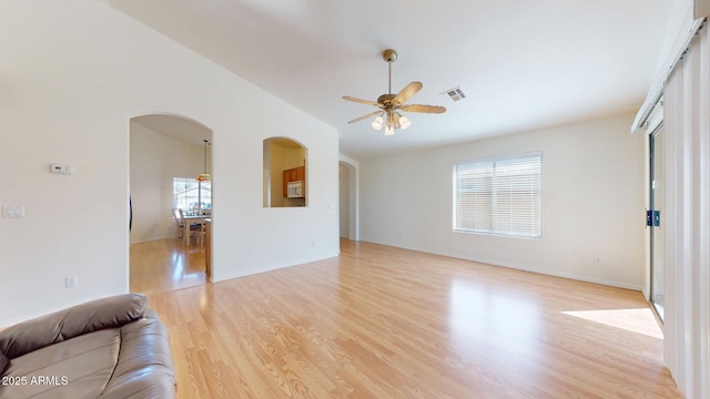 unfurnished living room featuring arched walkways, visible vents, light wood finished floors, and a ceiling fan