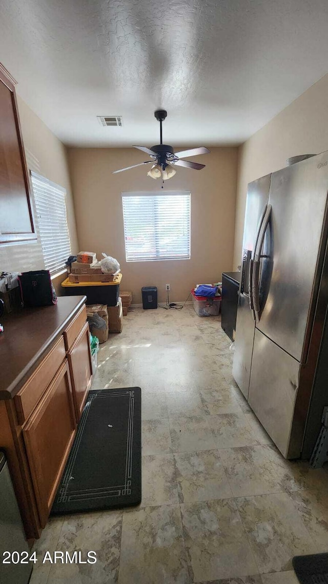 kitchen with a textured ceiling, stainless steel fridge, and ceiling fan